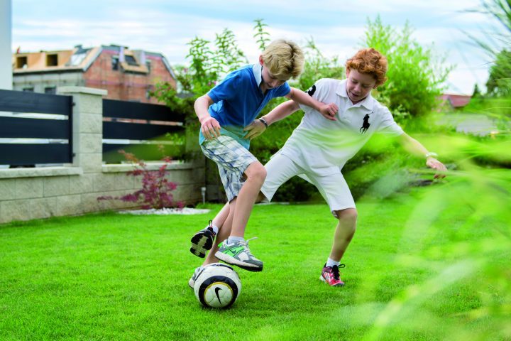 Man sieht zwei Kinder, die im Garten Fußball spielen.