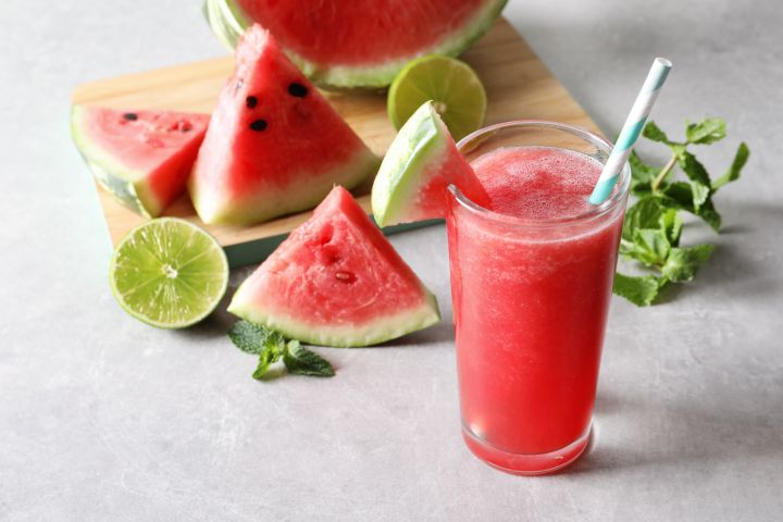 Man erkennt eine aufgeschnittene Wassermelone und ein Glas mit Wassermelonen-Saft.