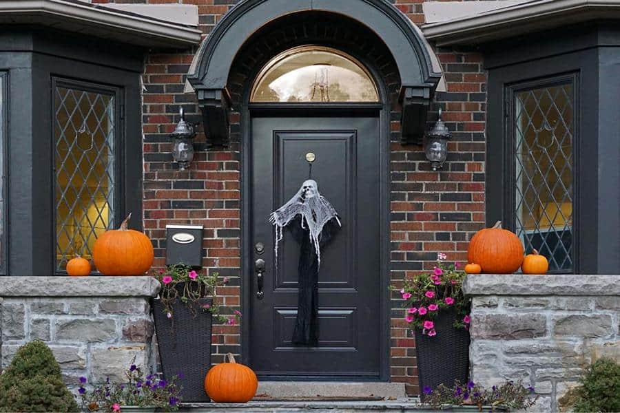 Halloween Dekoration im Eingangsbereich eines Hauses, auf der Haustüre hängt ein Gespenst, rundherum orange Kürbisse