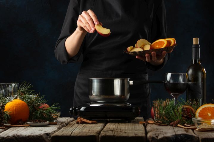 Koch bereitet Punsch zu, runderherum verschiedenste Zutaten, schwarzer Hintergrund