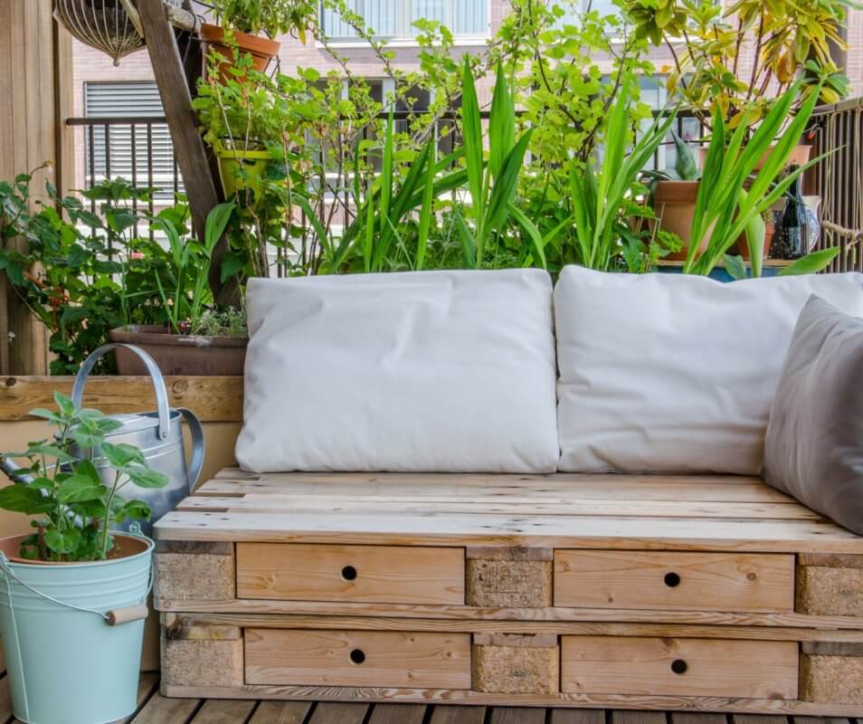Couch aus Palletten mit Sitzpolsterauflagen, dahinter grüne Pflanzen