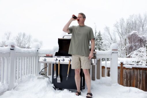 Grillen im Winter: Mann steht im Winter mit Bierflasche vor dem Griller
