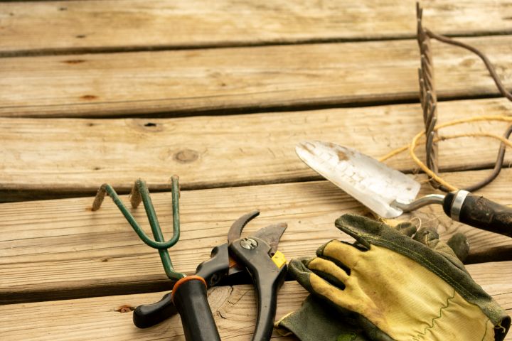 Gartengeräte: Rechen, Gartenhandschuhe, Gartenschaufel und Gartenschere liegen auf einer Holzterrasse