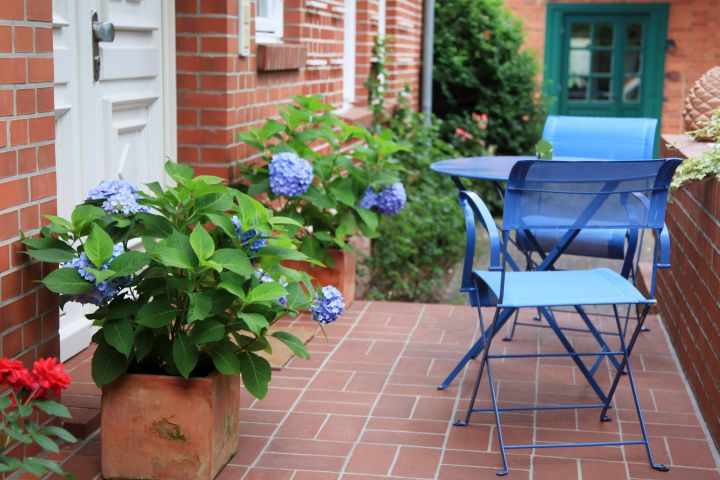 Terrassengestaltung: Terrasse gemütlich an einem Backsteinhaus mit blauen Hortensien und Terrassenmöbeln