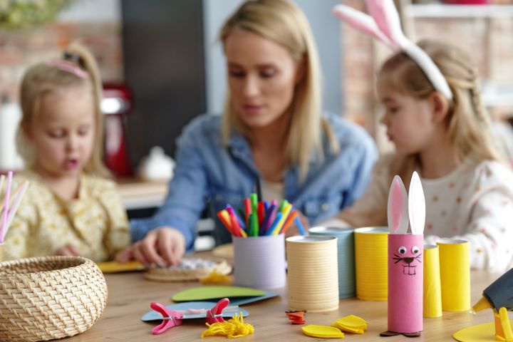 Mutter sitzt mit ihren beiden Töchtern am Tisch und bastelt Deko für Ostern