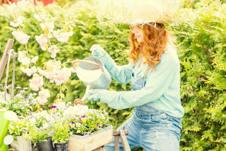 Frau gießt Blumen im Garten mit einer Gießkanne