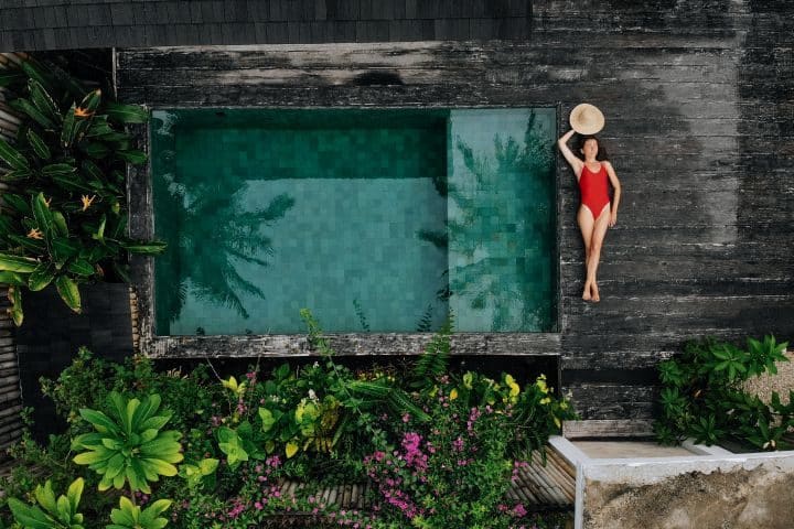 Frau in rotem Bikini liegt neben einem Naturpool