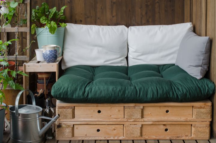 DIY Möbel für den Balkon, Sitzcouch gemacht aus Paletten, dekoriert mit einer grünen Auflage und weißen Kissen
