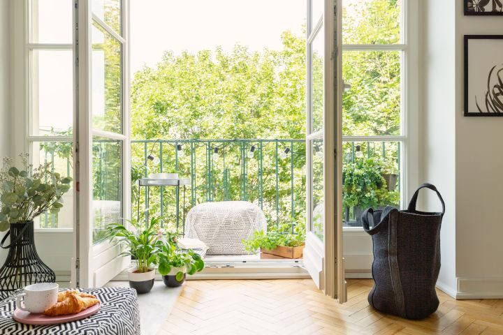Sicht durch geöffnete Balkontüren hinaus auf einen modernen Balkon und blühenden dahinterliegenden Garten